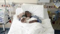 Child holding a teddy bear rests in hospital bed
